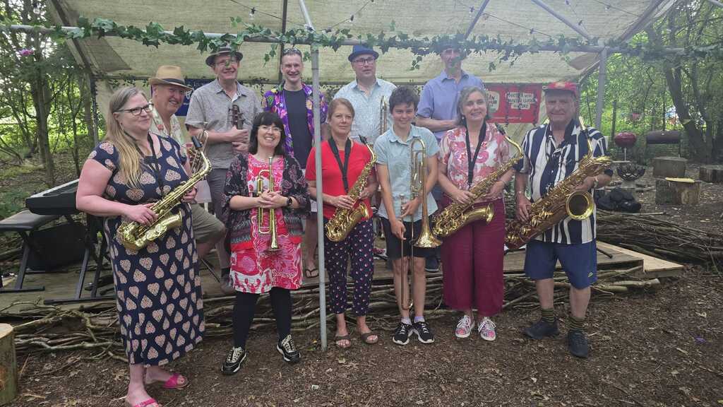 Picture of Jazz Band standing at the front of a makeshift stage in the middle of a forest. image