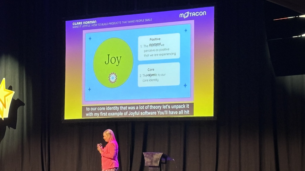 Clare onstage at Brighton Dome talking about building products with moments of joy. image