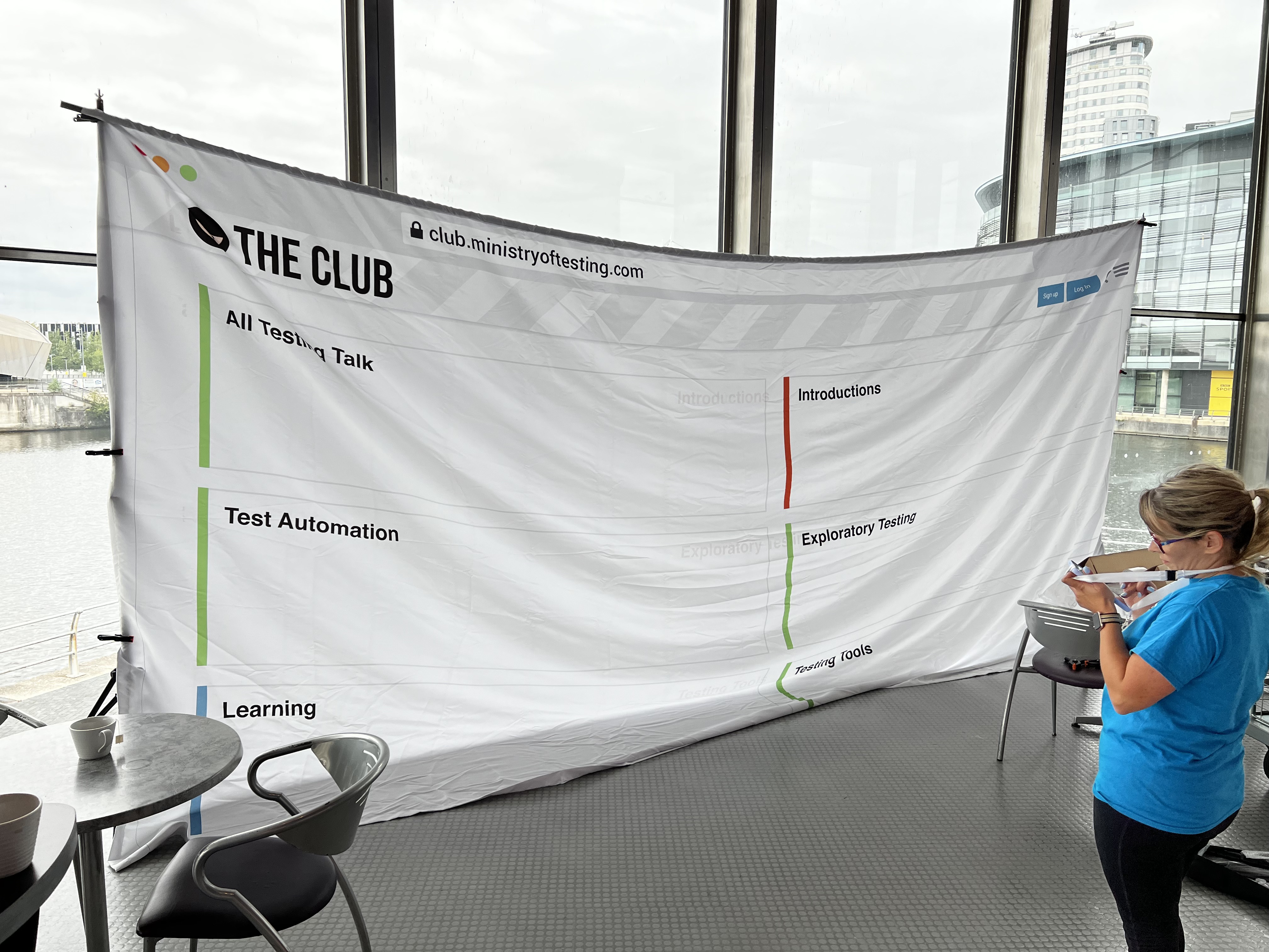 A woman stands to the right and in front of a massive sheet in a conference space.