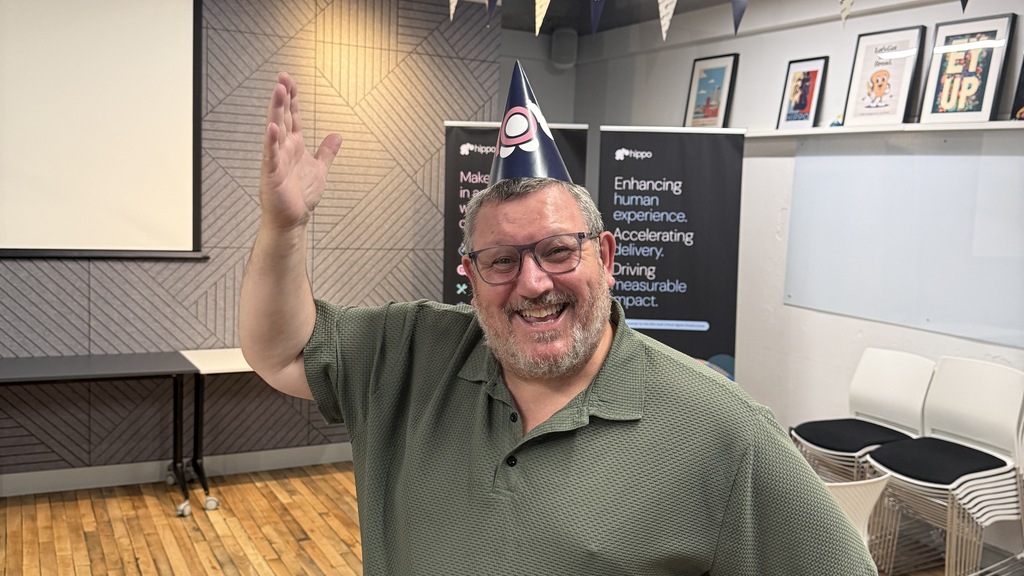 Ady Stokes with a 10 Hippo party hat pointing to a banner with Hippo 10 and logos  image