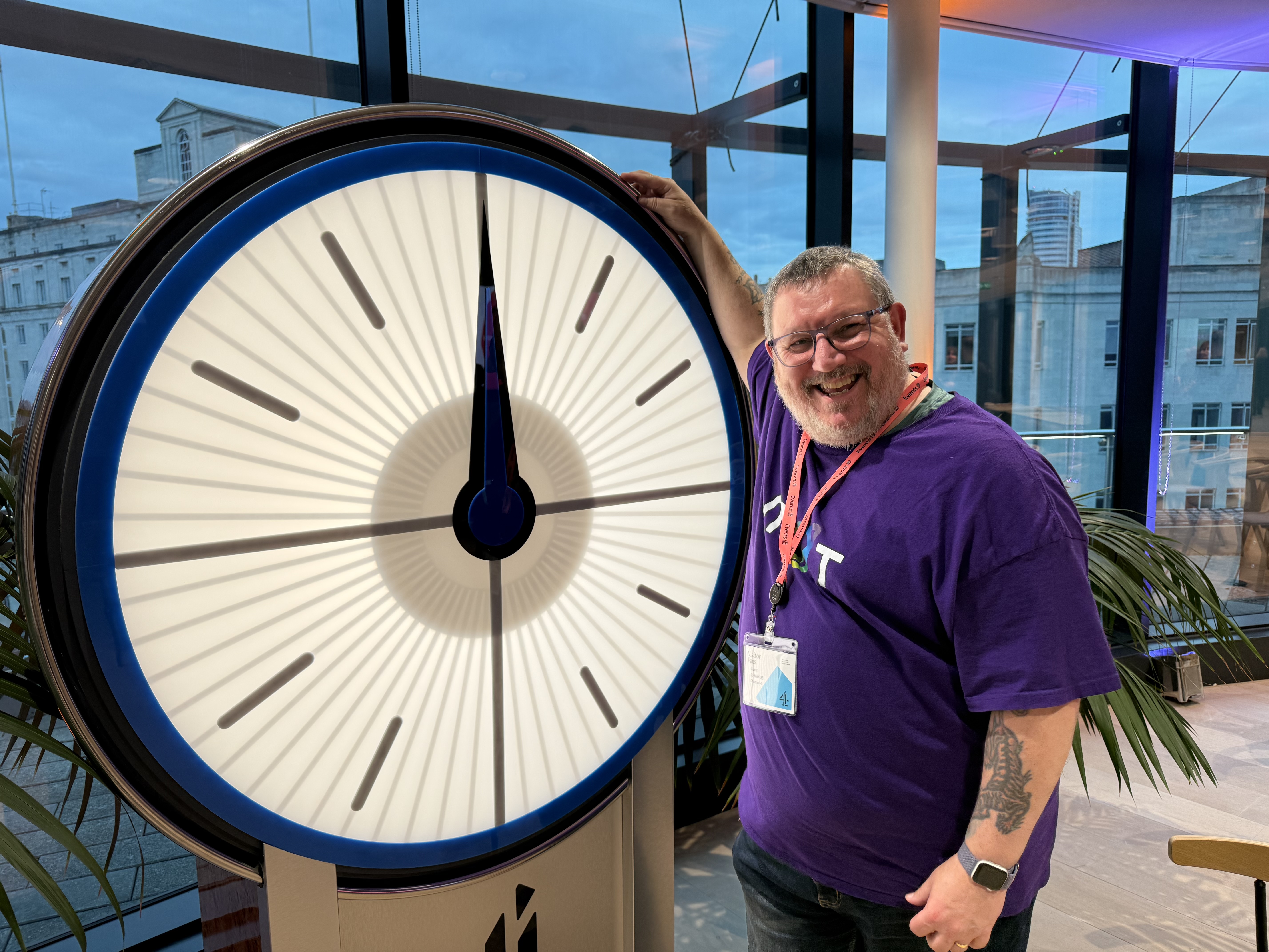 Ady in a MoT purple T-shirt with a rainbow logo is stood in front of the channel 4 countdown clock from the TV quiz.  image