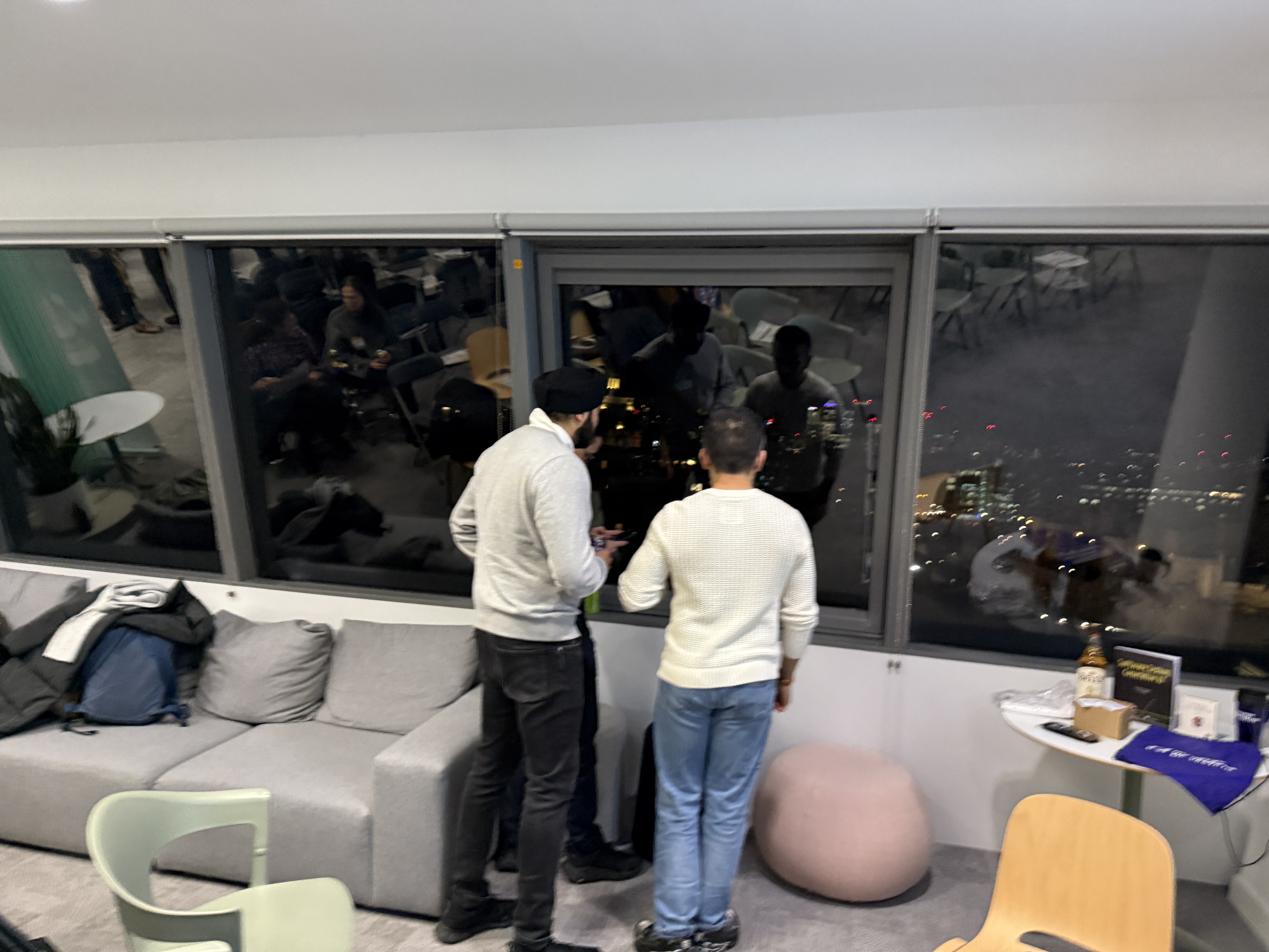 Three people stand at a window looking out at a city view.