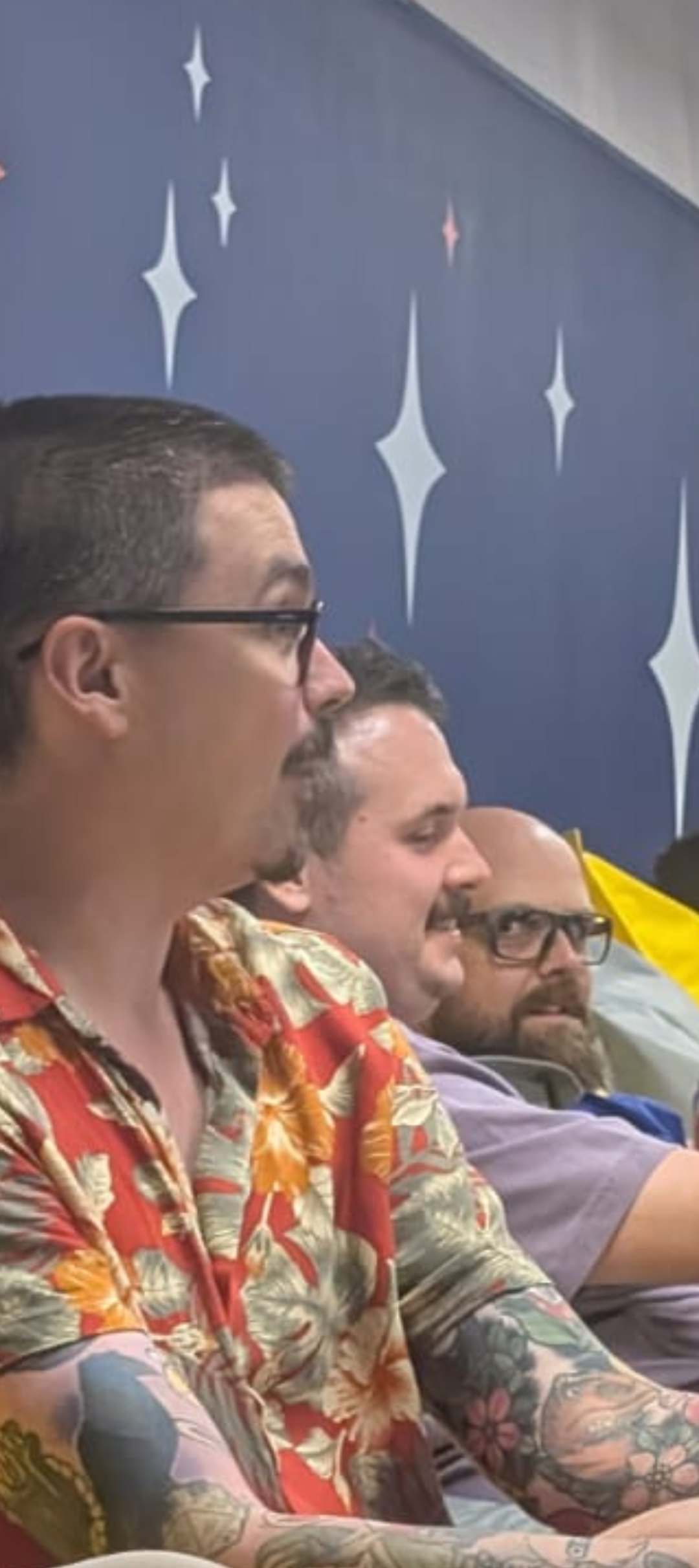 Image of three guests at a meetup. Callum akehurst Ryan looking interested in a talk. To their right a security engineer making a face, to that person's right Tom is making a face with a strong gaze at the security engineer that is funny and wide eyed.