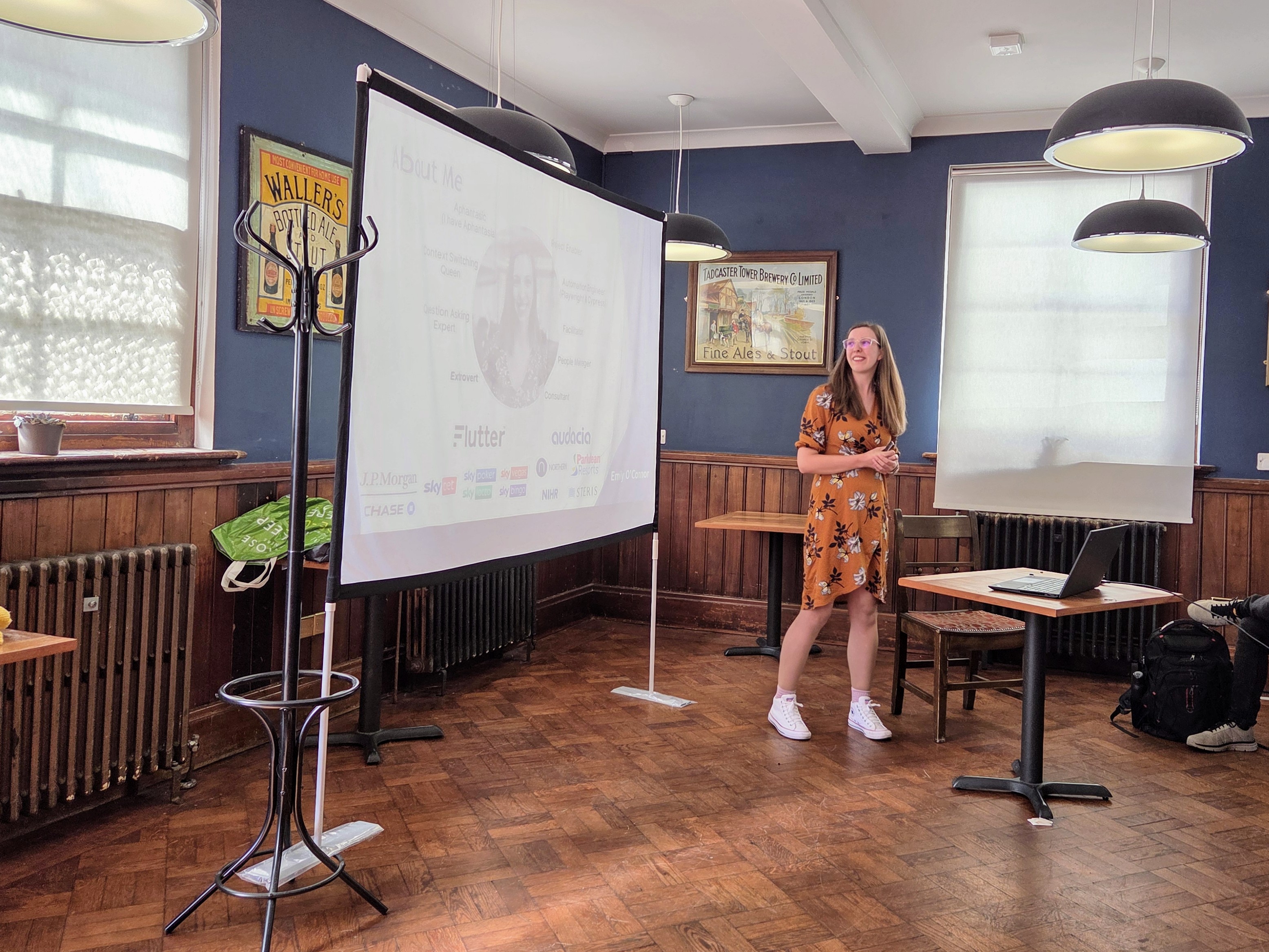 Emily O’Connor standing beside a projector screen during her talk at Leeds Testing Atelier, speaking to a full audience.