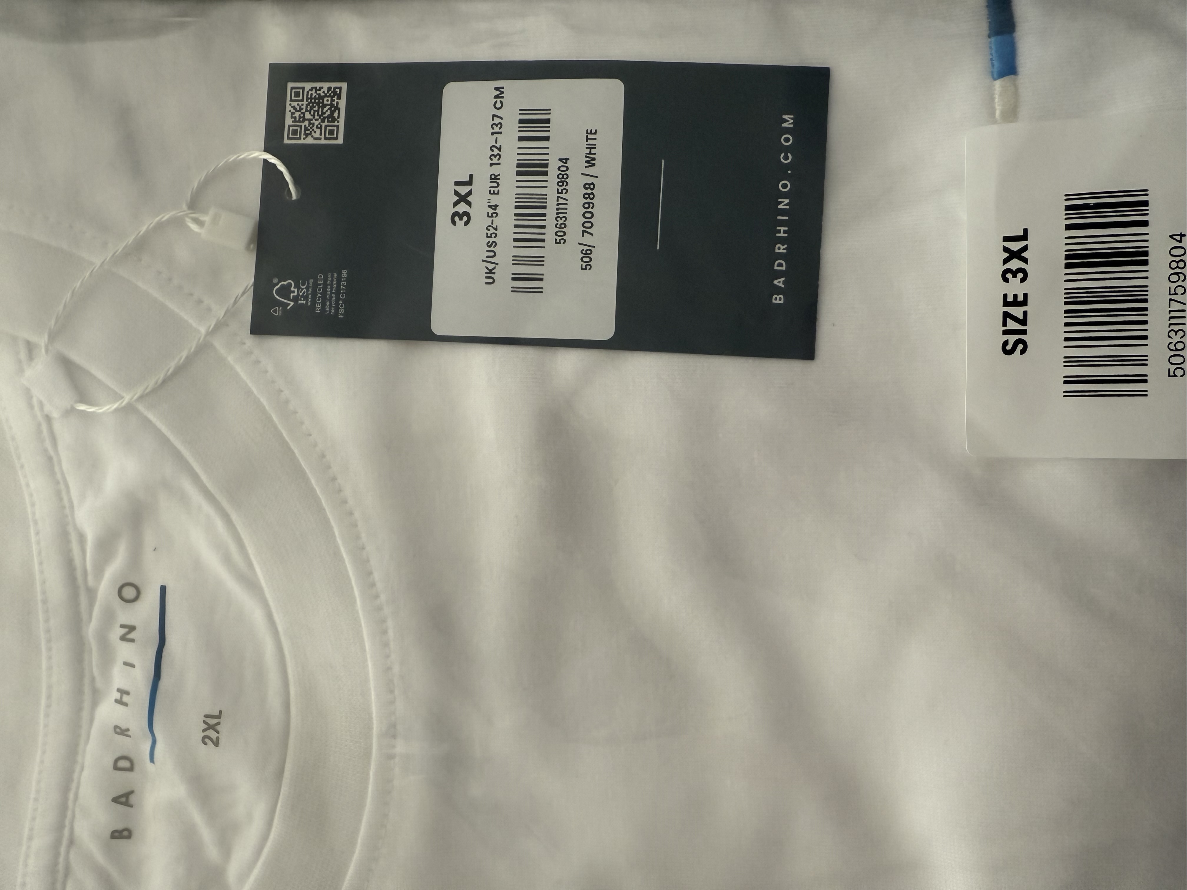 White T-shirt in clear packaging. A tag says 3xl, a sticker says 3xl, the T-shirt on the back inside the collar says 2xl 