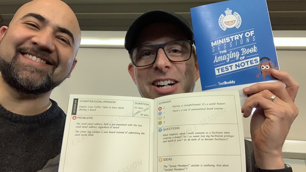 Two men, looking very happy holding up a physical notebook with the following words on the front cover: Ministry of Sessions: The Amazing Book of Test Notes