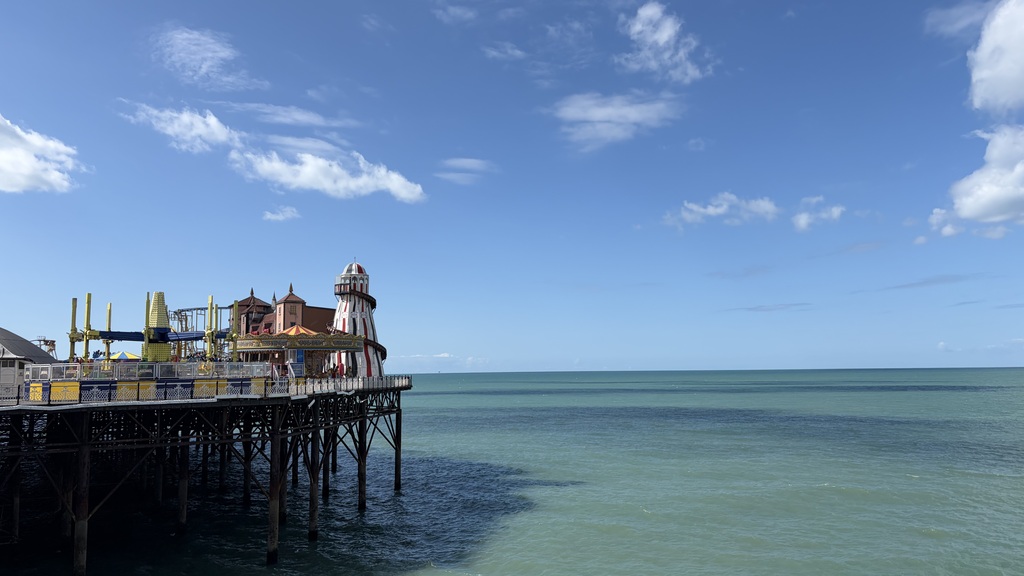 Photo of blue sky and sea at Brighton Palace Pier. There are fun fair rides to the left. image