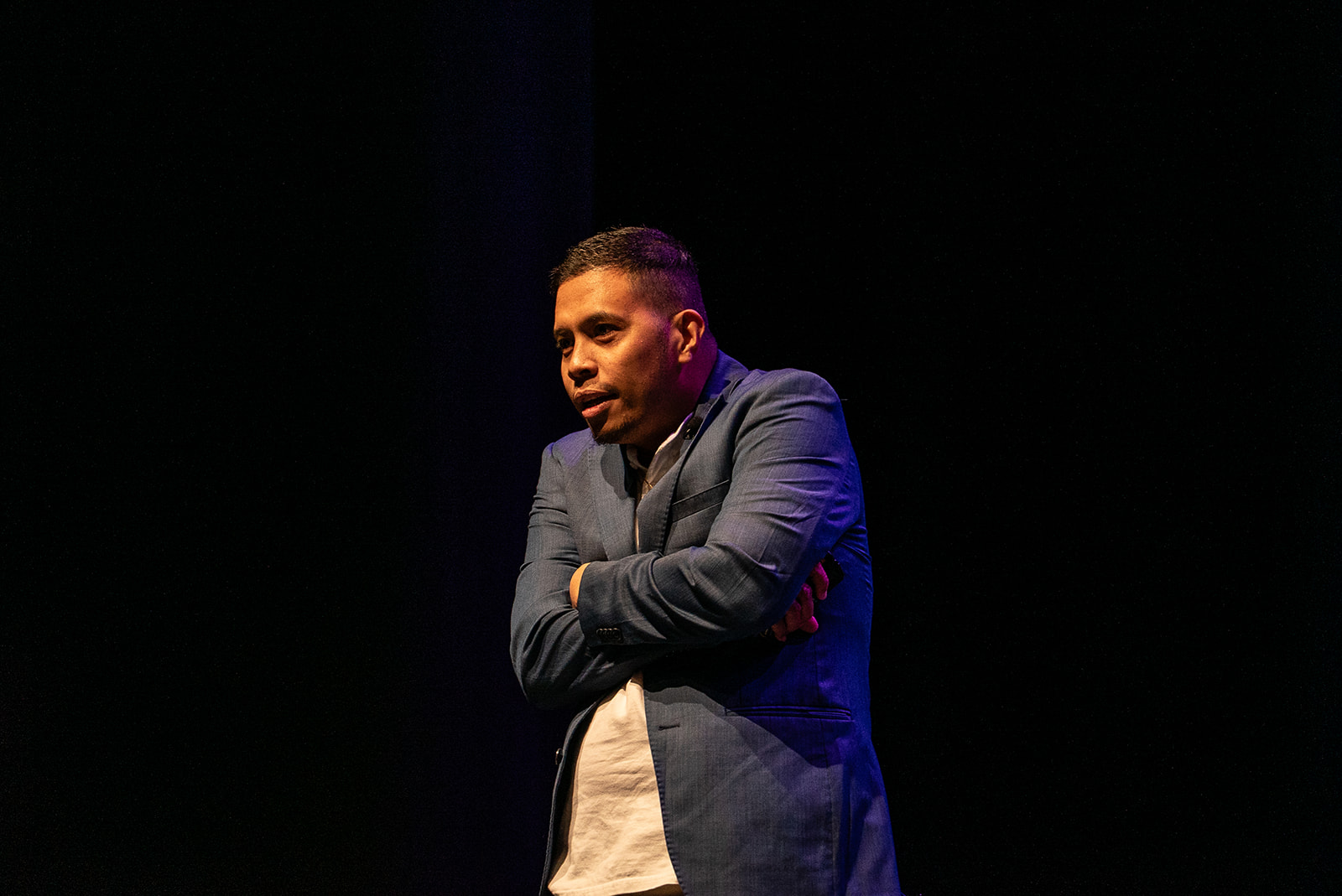 Kulas Angeles on stage with an expressive crossed arms gesture.