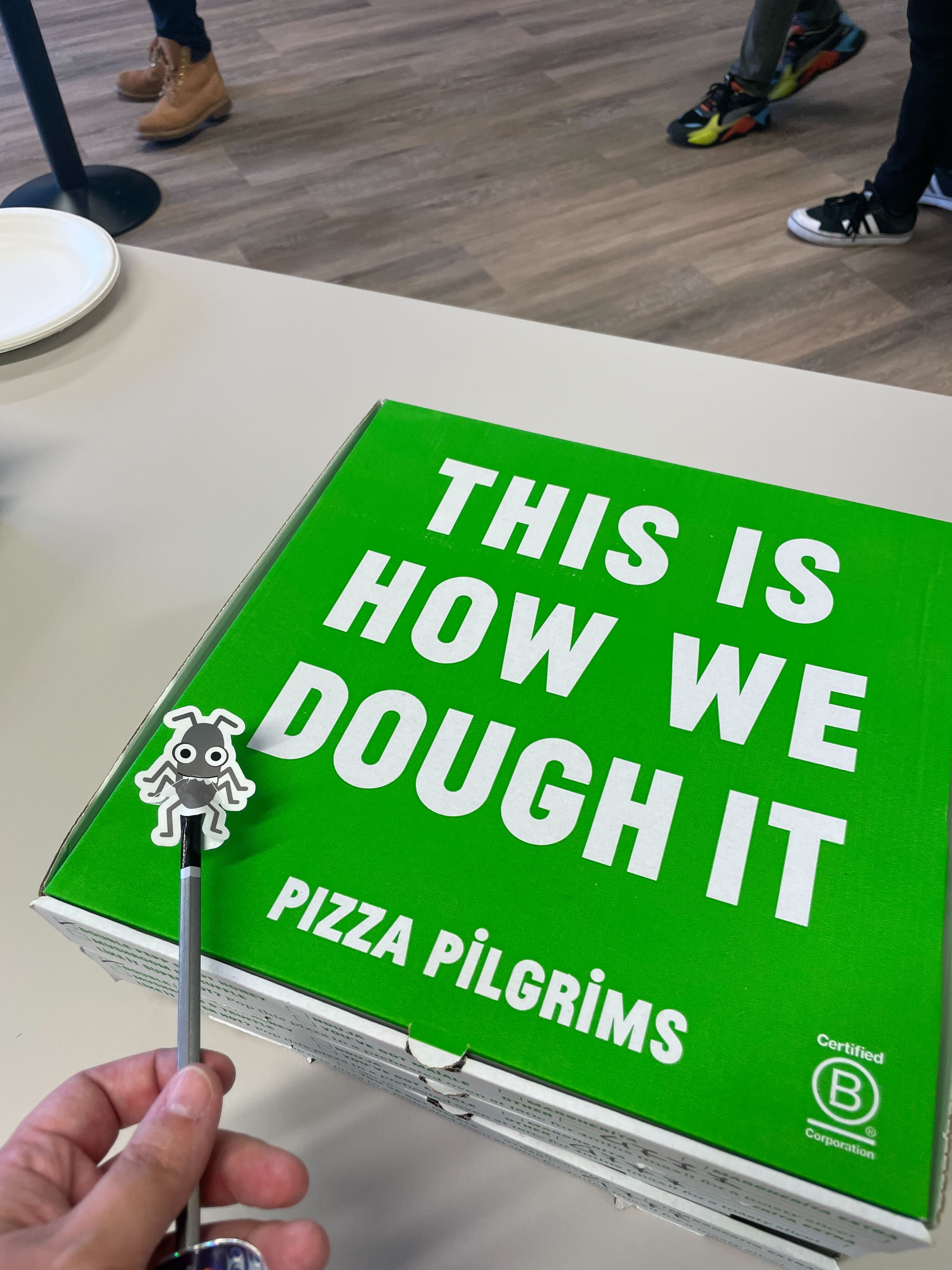 A photo of a pizza box that says 'This is how we dough it. Pizza Pilgrims'. Bug sneaks in to be included in the shot too.