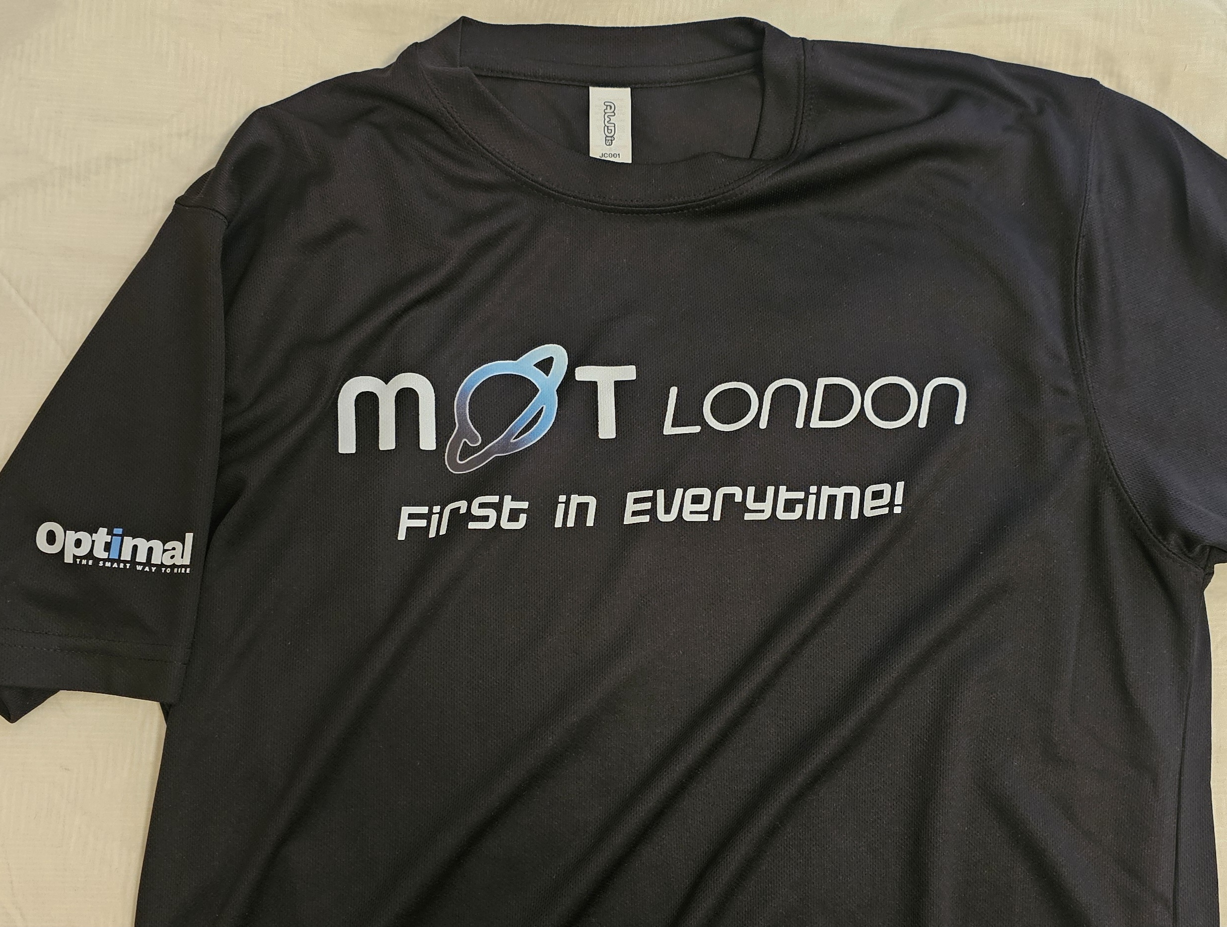 A navy t-shirt with the words "MOT LONDON - FIRST IN EVERYTIME' on the front.

On the sleeve is the logo for Optimal recuitment.
