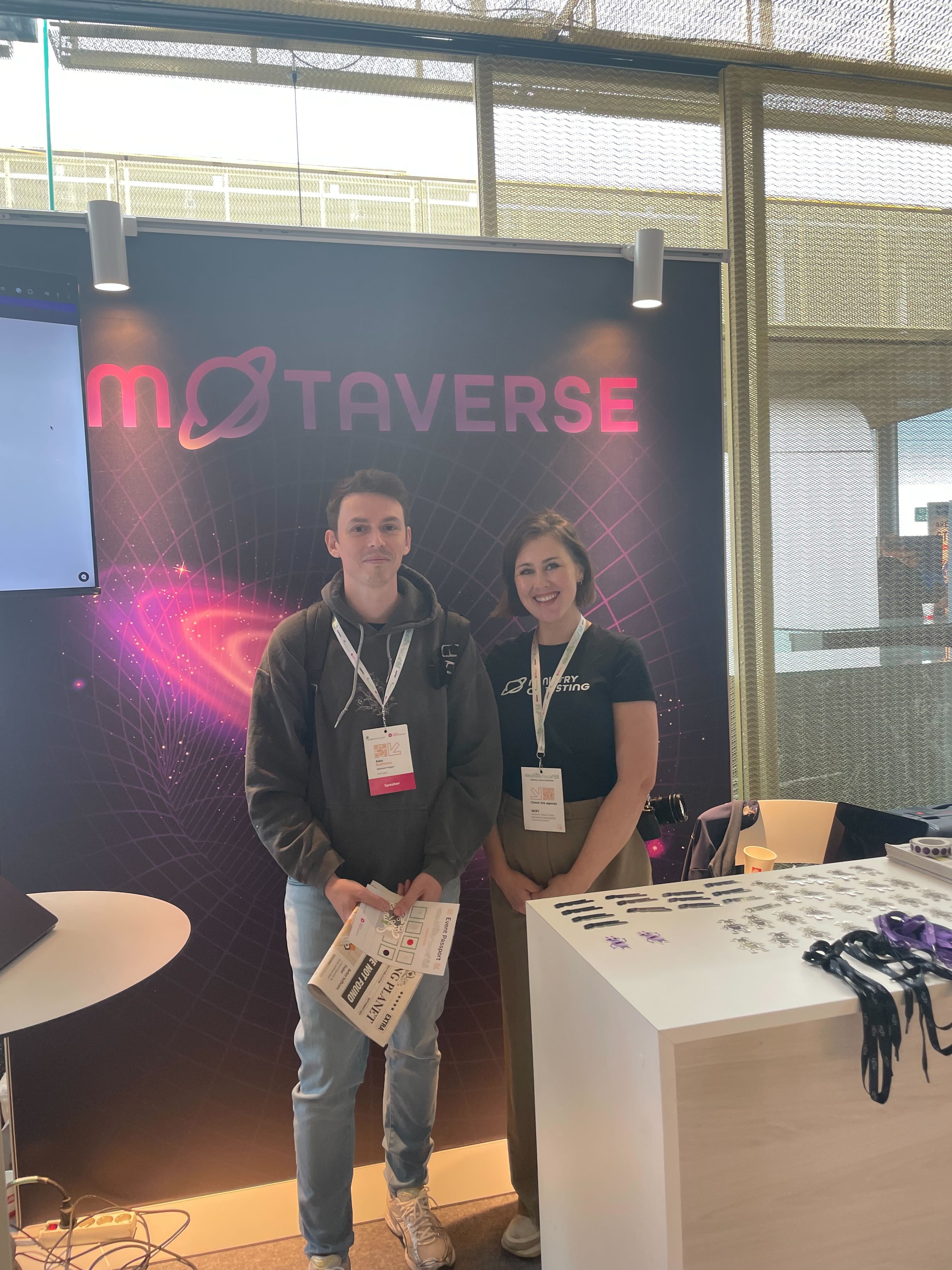 Alex and Alex pose in front of the MoTaverse banner.