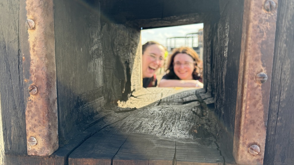 Two women looking through a wooden structure. image