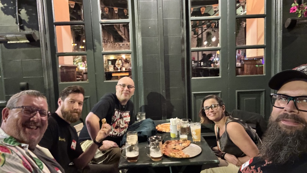 Five friends gathered around a table in a cozy pub, smiling at the camera over pizza and glasses of beer. Dark green ... image