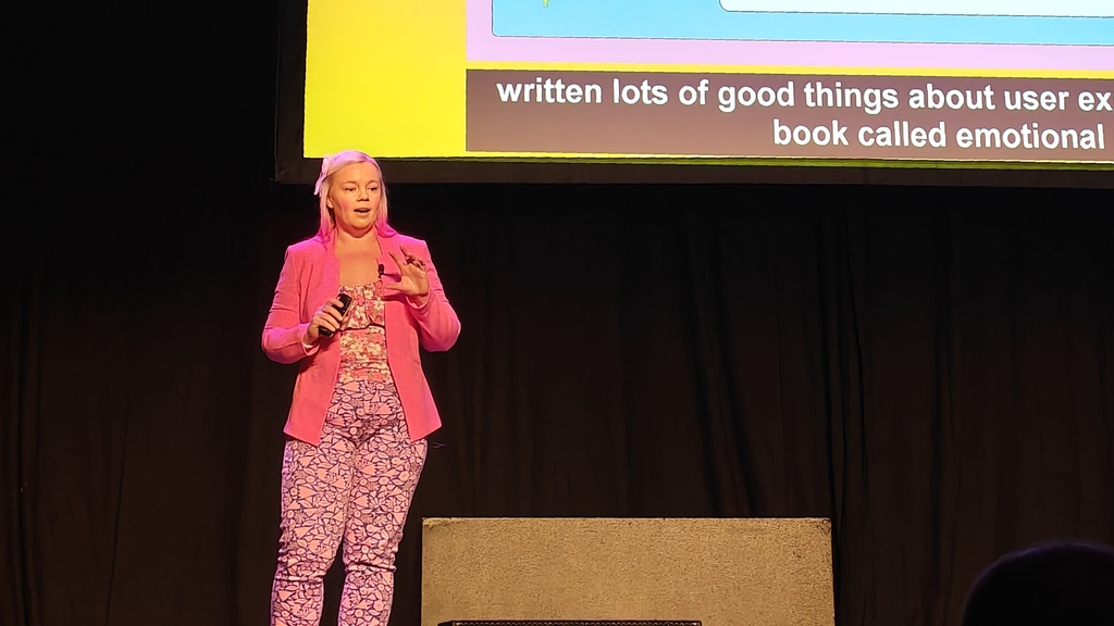 Clare presenting her talk on stage. She is decked out in her favoured pink and presenting joyfully image