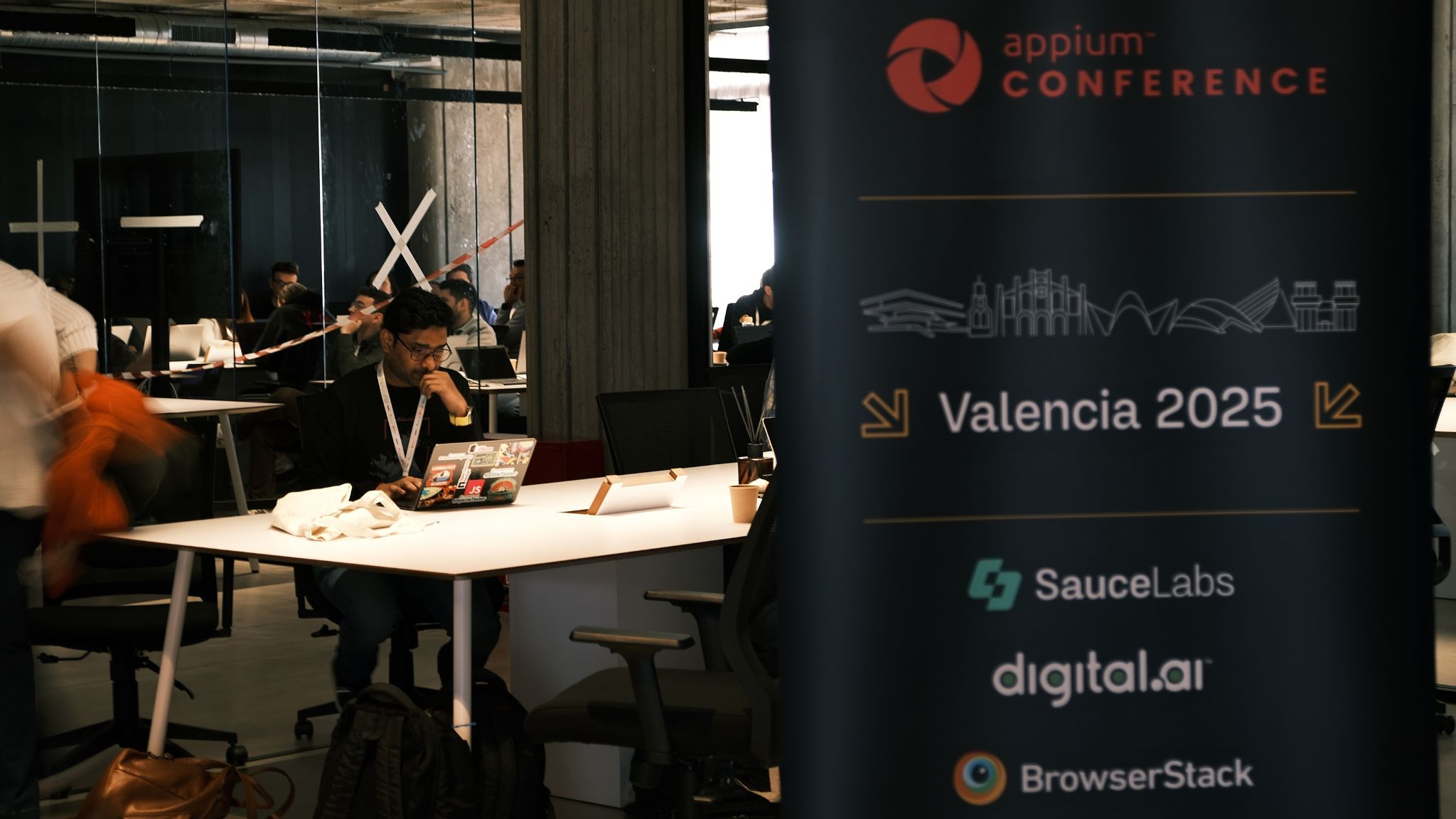 Close-up of a conference attendee working on a laptop in the workshop space. The conference banner is partially visible, showing "Appium Conference, Valencia 2025" and sponsor logos.